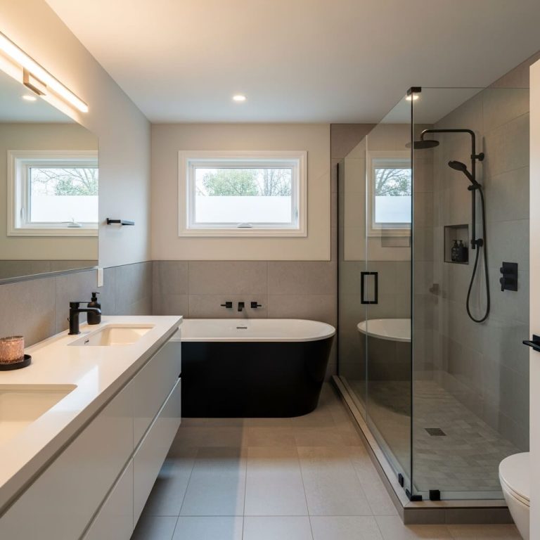 Baño moderno con ducha, bañera negra y lavabo con mueble blanco. Luz natural.