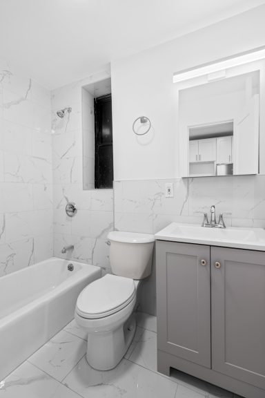 Baño minimalista en tonos blancos con bañera, inodoro y lavabo moderno.