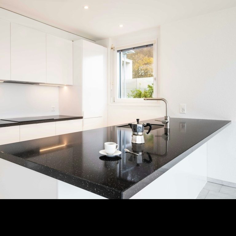 Cocina moderna con muebles blancos y encimera negra, iluminación brillante y ventana.