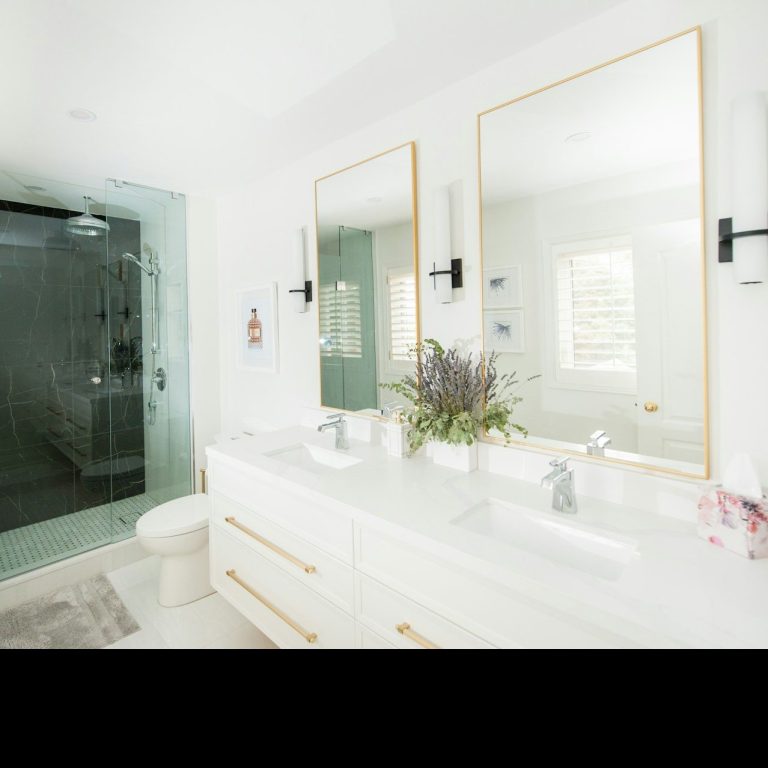 Baño moderno con espejos dorados, ducha de vidrio y decoración minimalista.