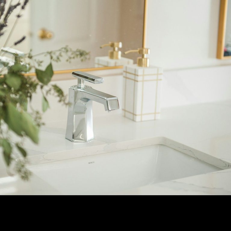 Grifo moderno sobre un lavabo blanco con plantas decorativas al fondo.