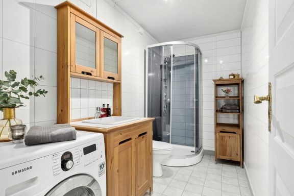 Baño moderno con ducha, lavadora y muebles de madera clara.