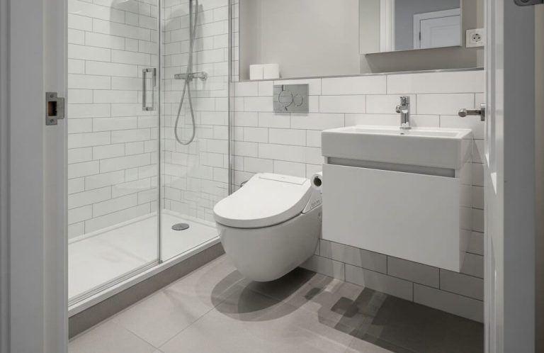 Baño moderno con ducha, inodoro y lavabo, revestido de azulejos blancos.