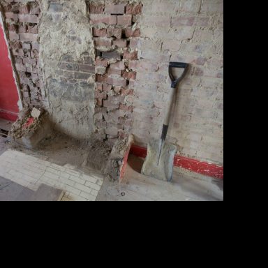 Pared de ladrillos expuestos con herramientas de jardinería al lado.