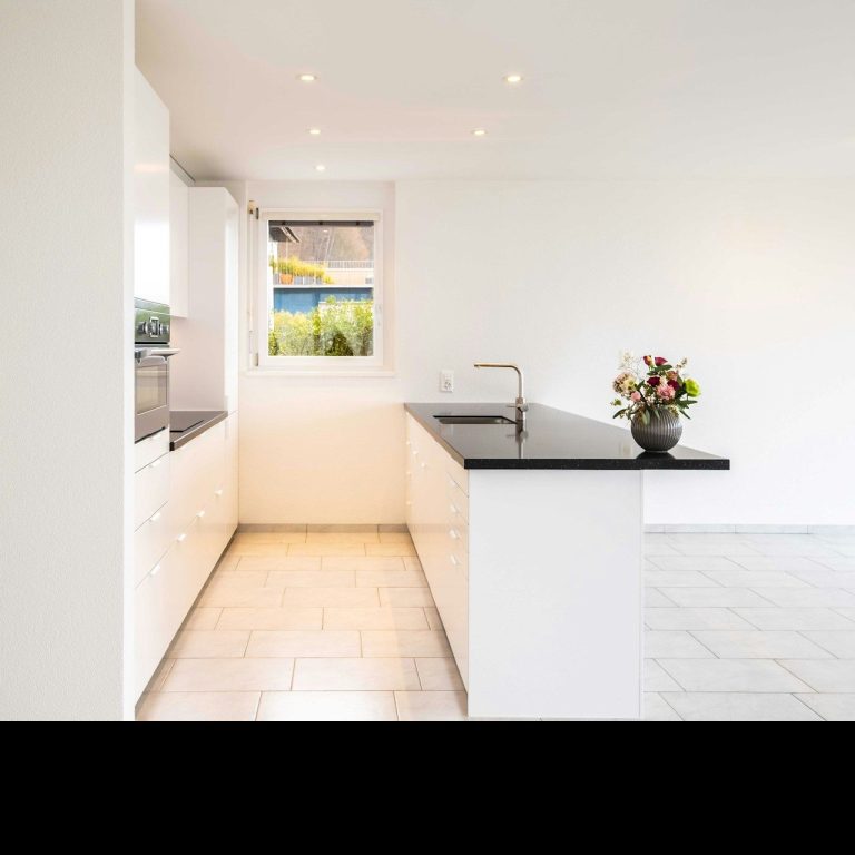 Cocina moderna y minimalista con encimera negra y ventana que da a un paisaje exterior.