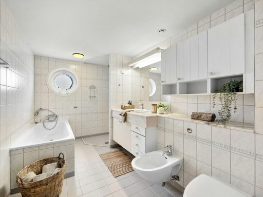 Baño moderno con bañera, bidé y mueble de lavabo, decorado con azulejos claros.